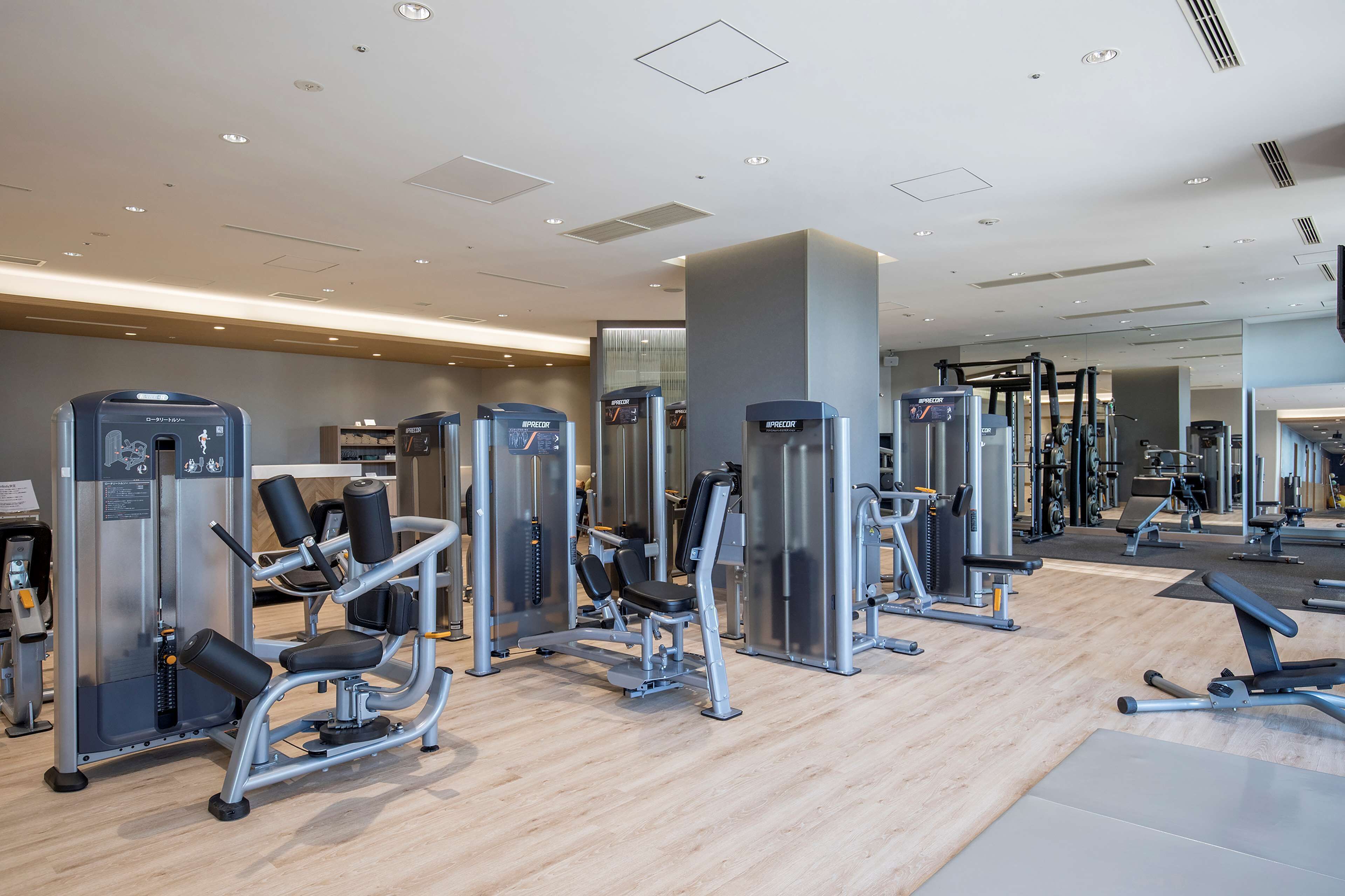 Un gimnasio moderno con diversas máquinas de ejercicio, suelo de madera y pared espejada.