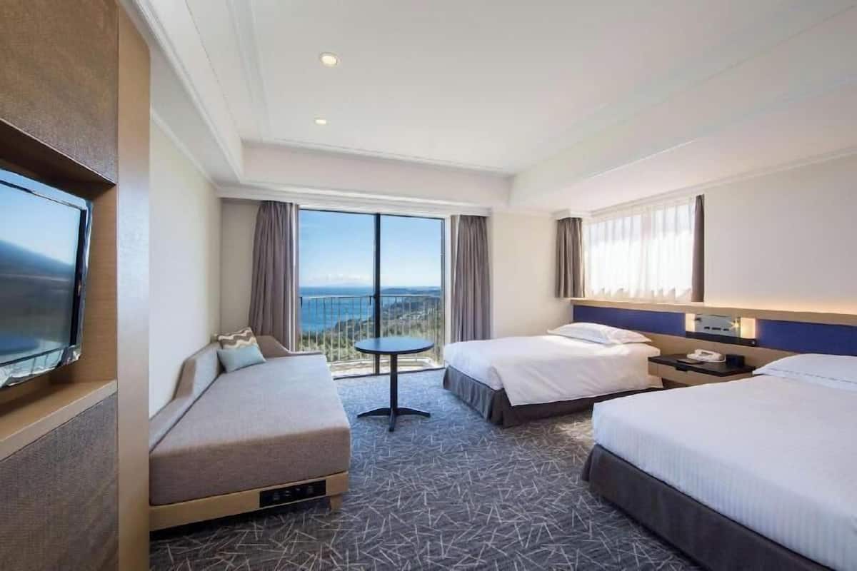A hotel room with two beds, a TV, a small table, and a balcony with a view.