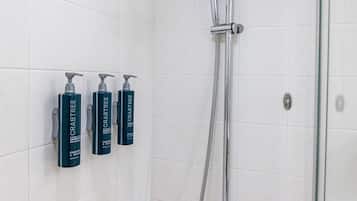 A shower area with a glass door, a handheld showerhead, and three bottles of Crabtree shower gel.