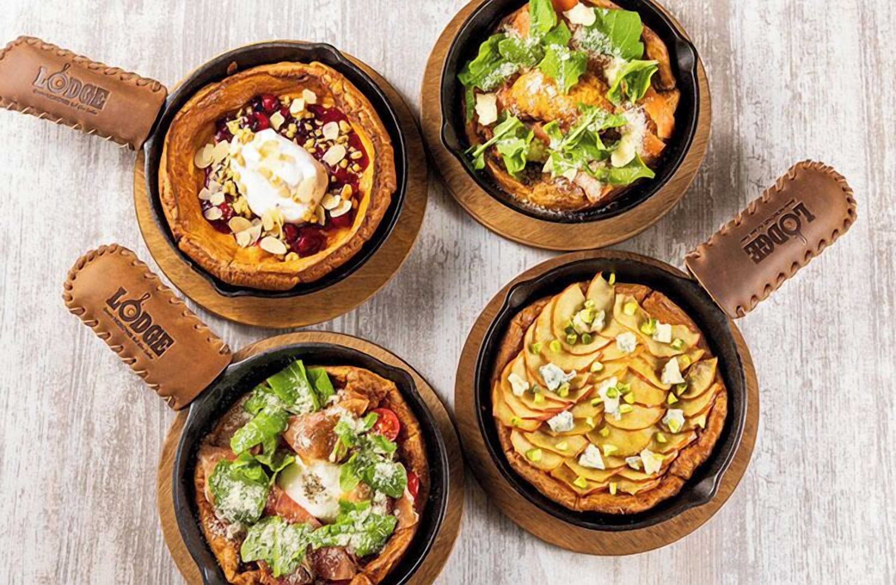 Four dishes served in cast iron skillets on a wooden table.