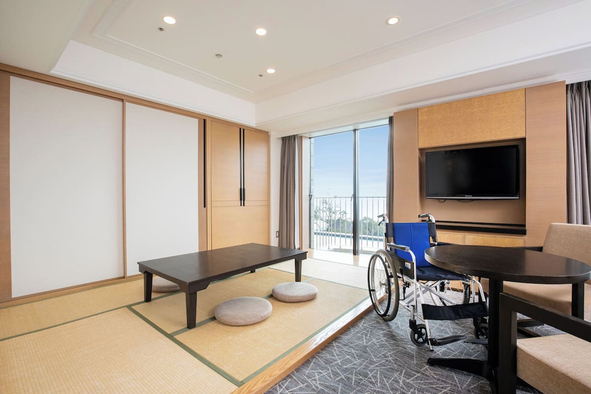 A hotel room with tatami flooring, a wheelchair-accessible table, a television, and a view of the outdoors.