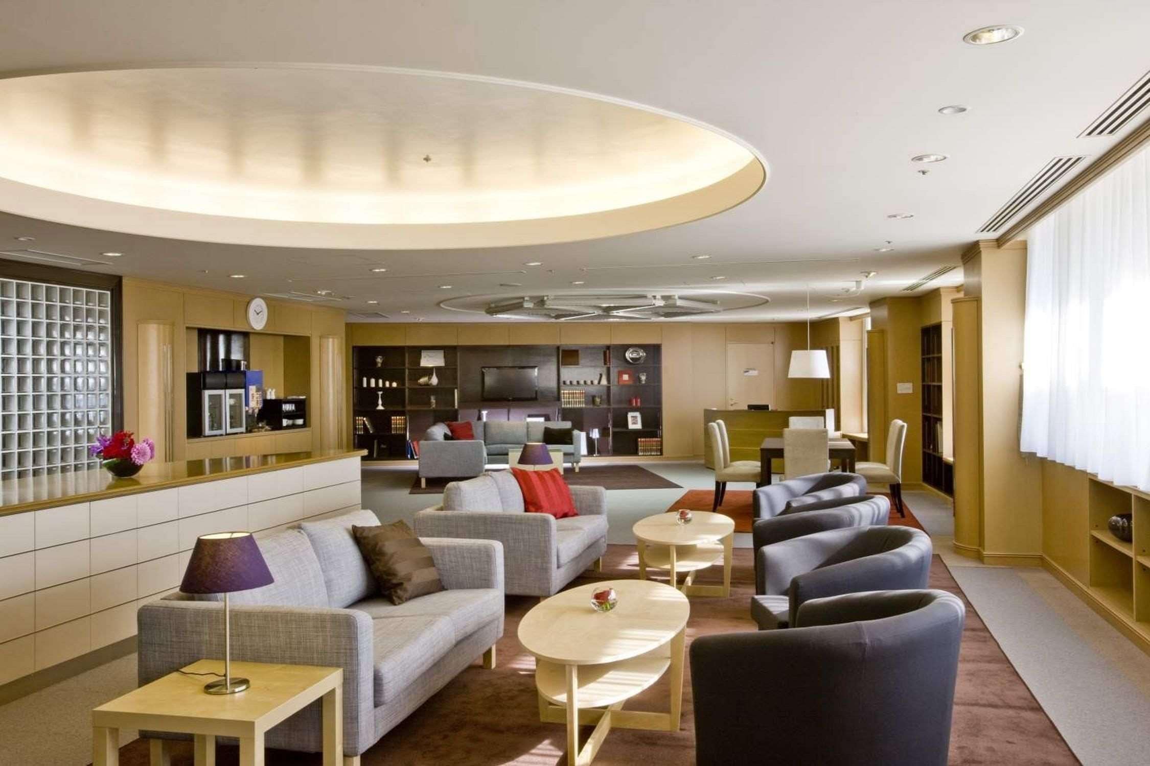 Un hall d’hôtel moderne avec un canapé, des fauteuils, une table basse, un téléviseur et une bibliothèque.