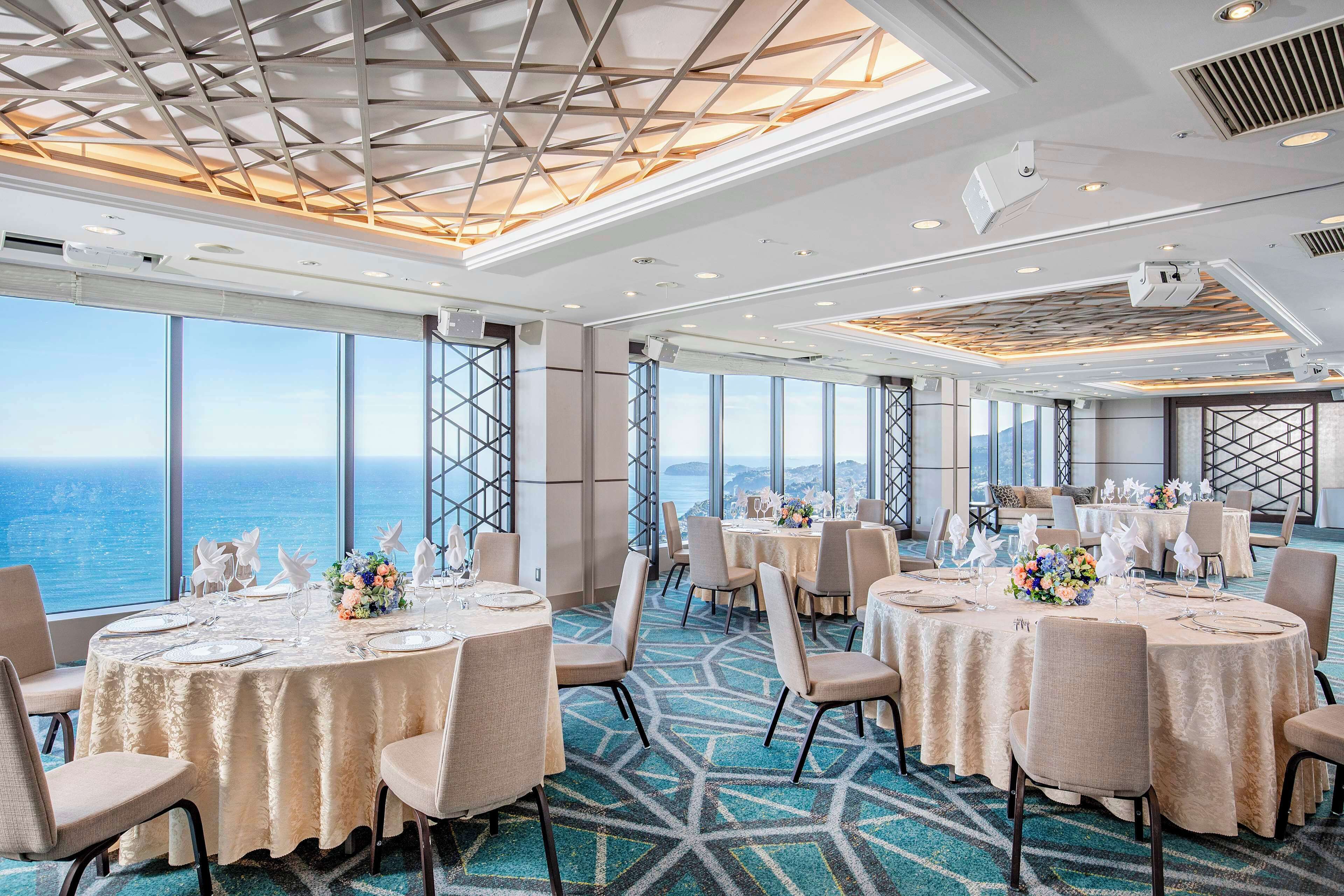 A spacious dining area with round tables, chairs, and a view of the ocean.