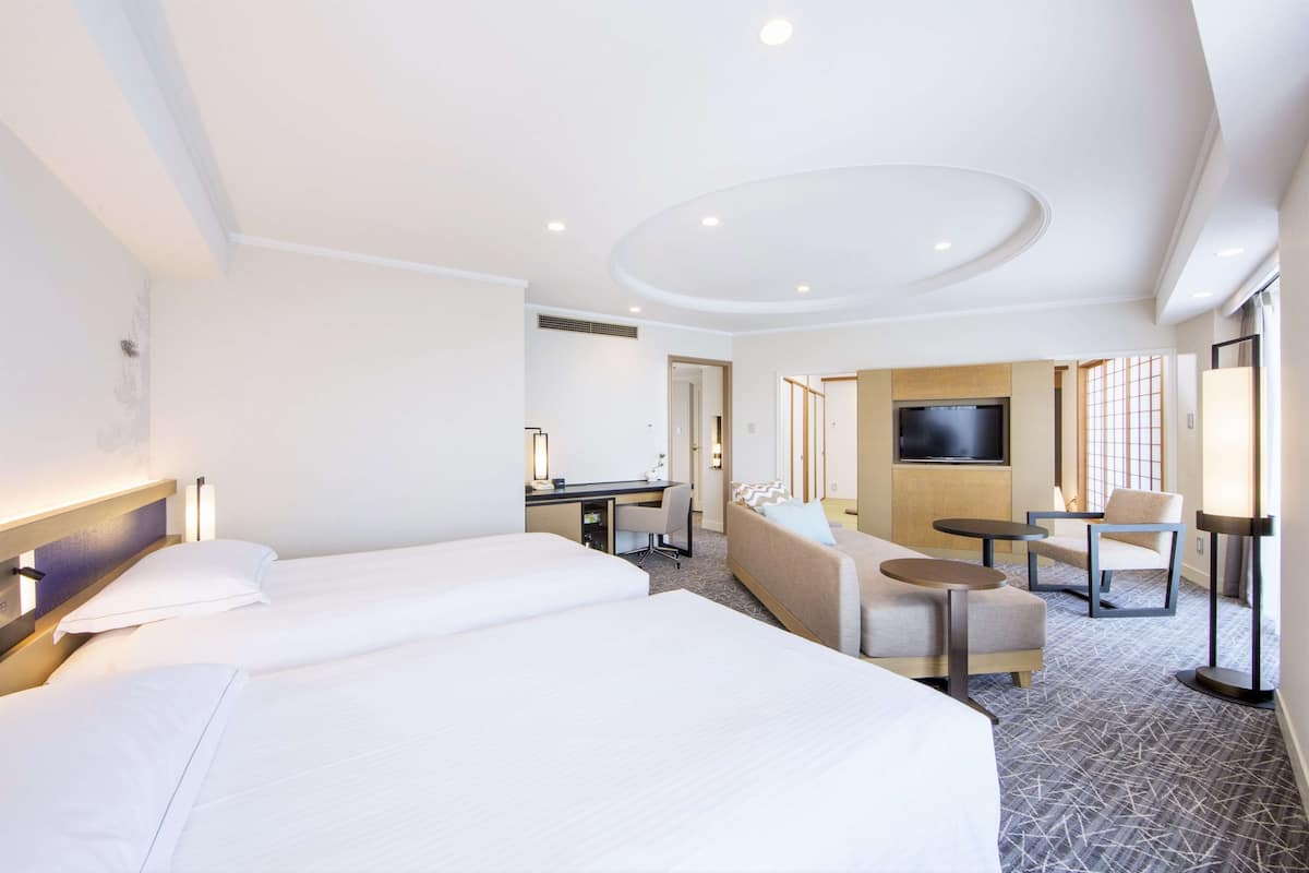 A hotel room with two beds, a sofa, a desk, and a TV.