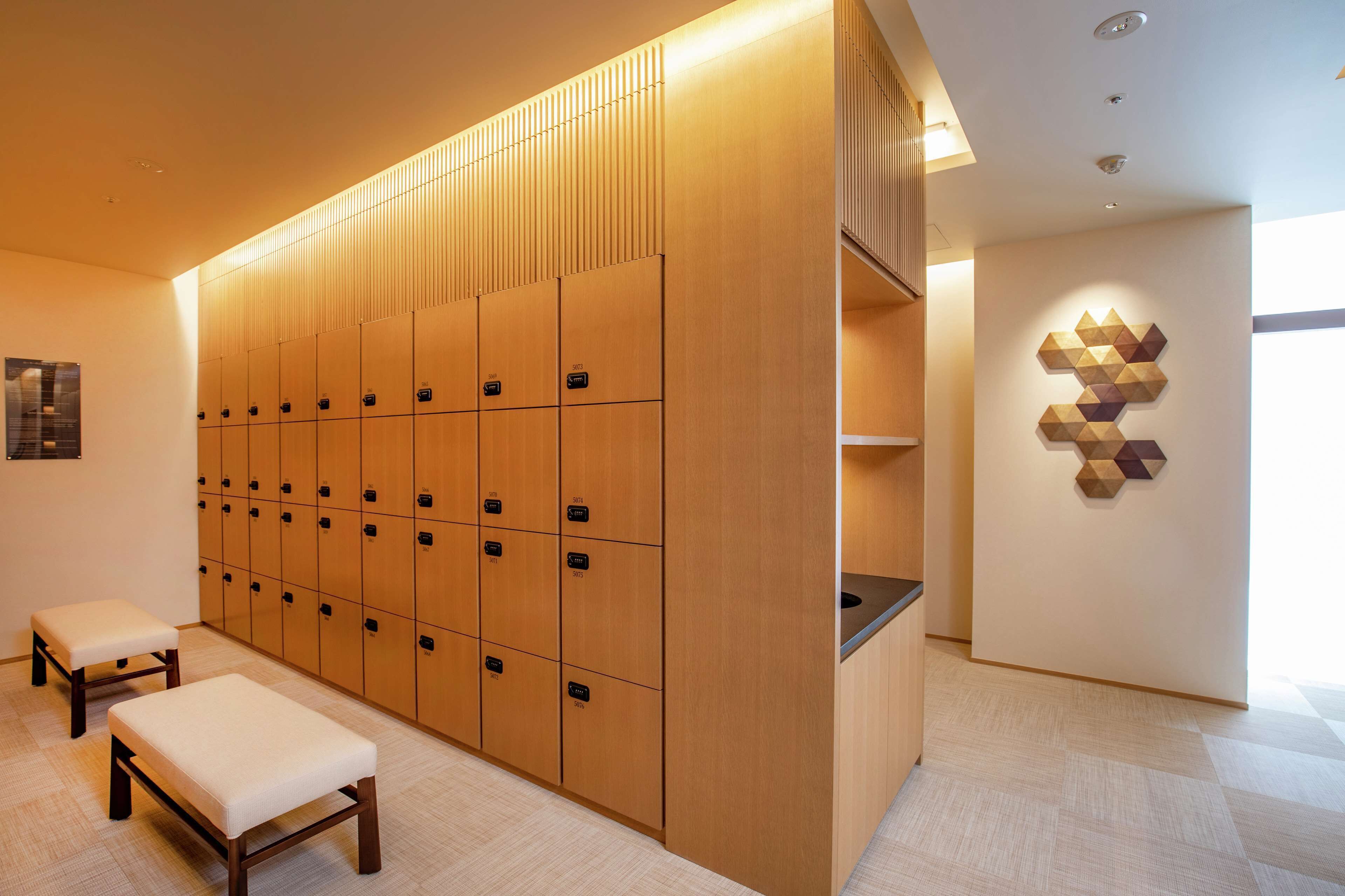 A modern locker room with wooden lockers, benches, and a geometric wall art piece.