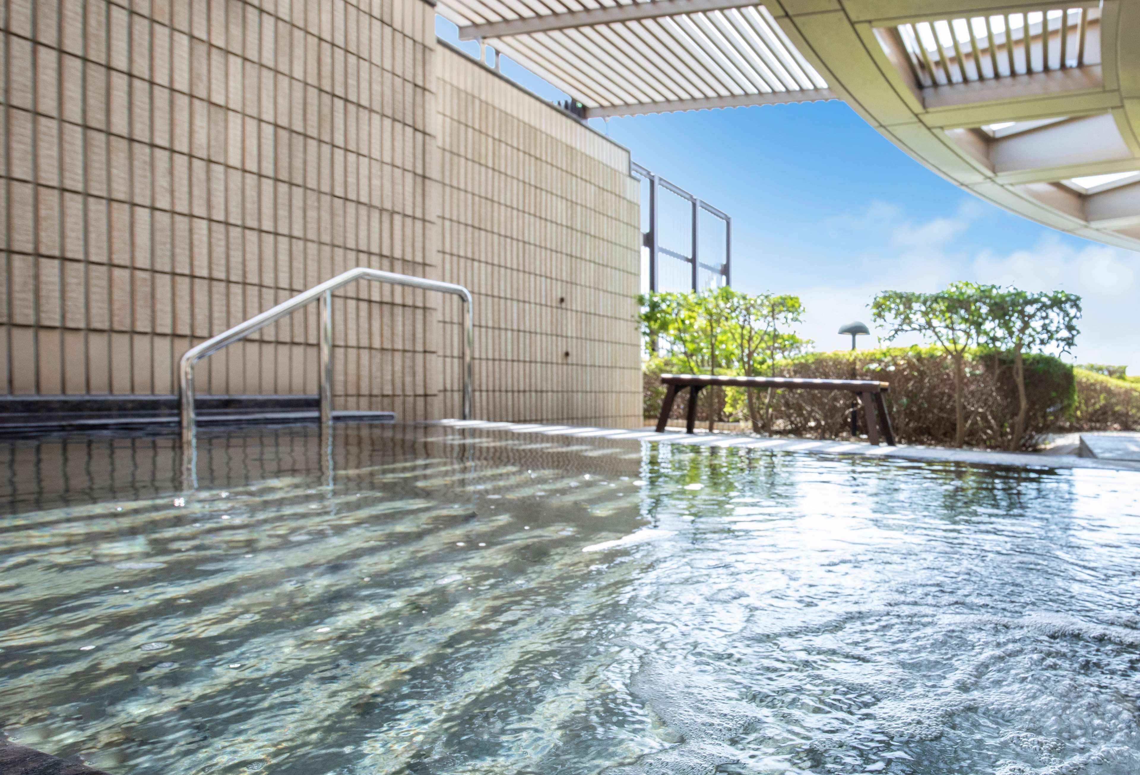 A swimming pool with clear water, a metal ladder, and a bench.