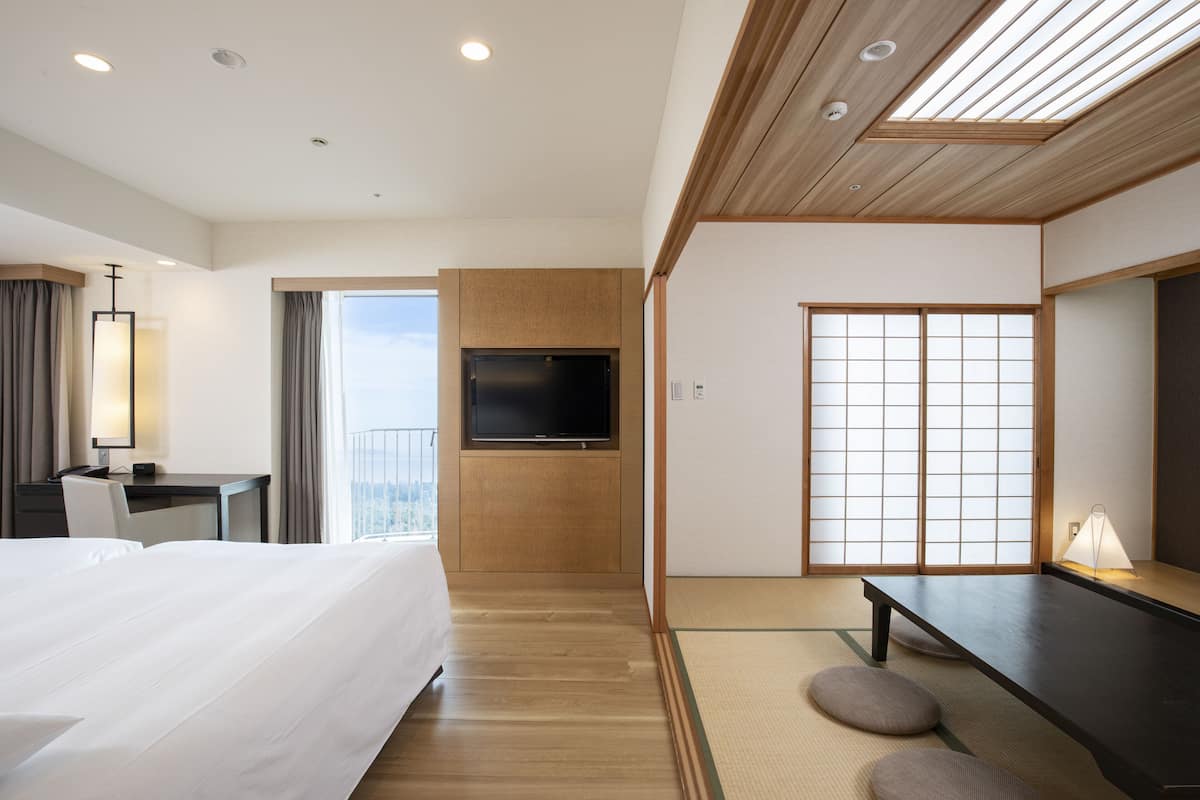 A hotel room with a bed, desk, TV, tatami mat, and sliding doors.