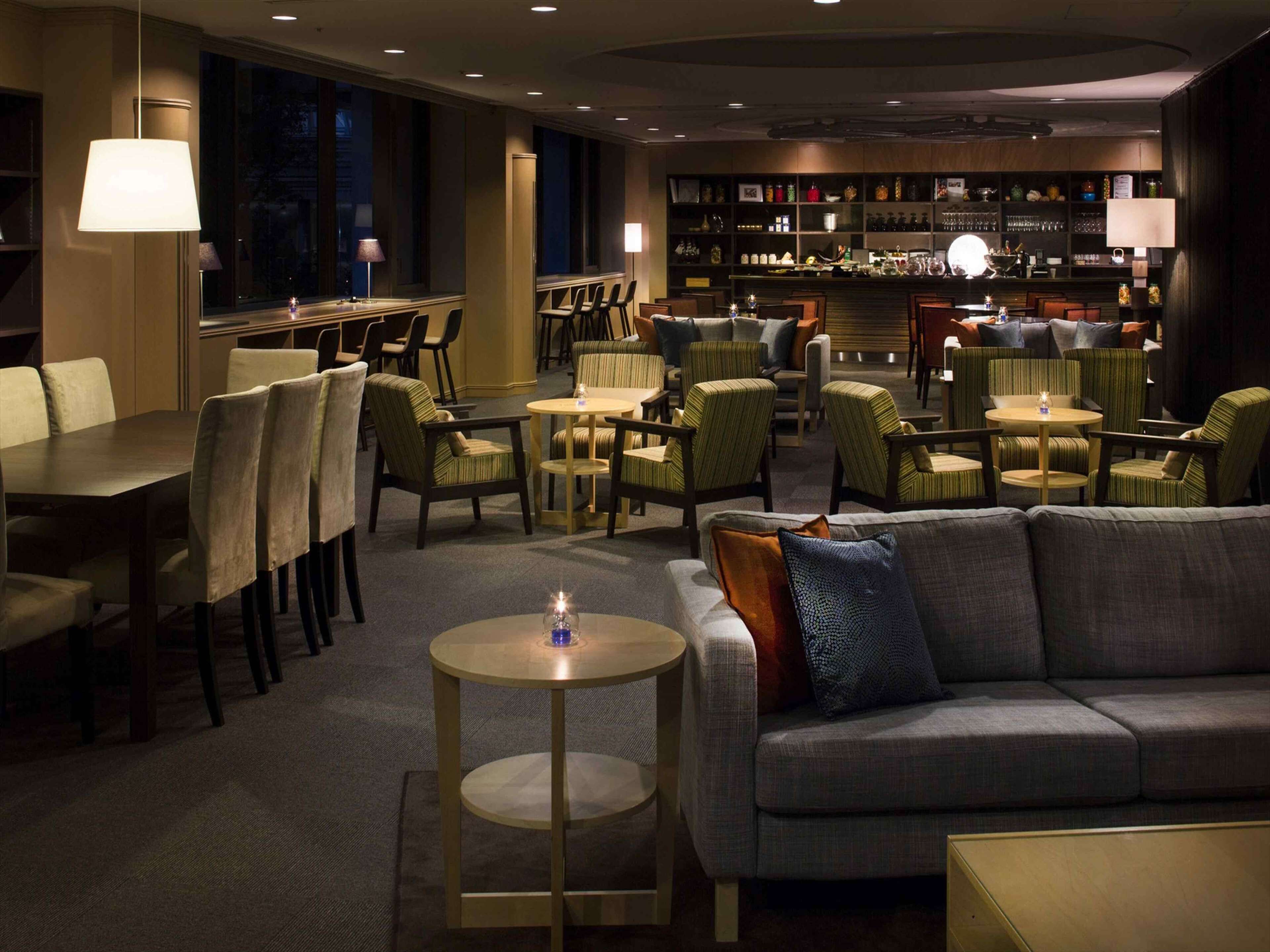 Un hall d’hôtel comprenant un bar, des espaces aménagés avec des sièges et un comptoir de réception.