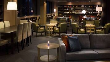 Un hall d’hôtel comprenant un bar, des espaces aménagés avec des sièges et un comptoir de réception.