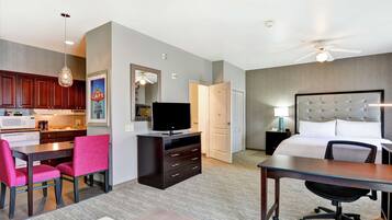 Une chambre d’hôtel équipée d’une kitchenette, d’un coin repas avec une table et des chaises, d’un lit avec une tête de lit, d’un bureau avec une chaise et d’un ventilateur de plafond.