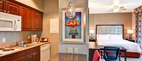 A hotel room with a bed, desk, chair, and kitchenette.