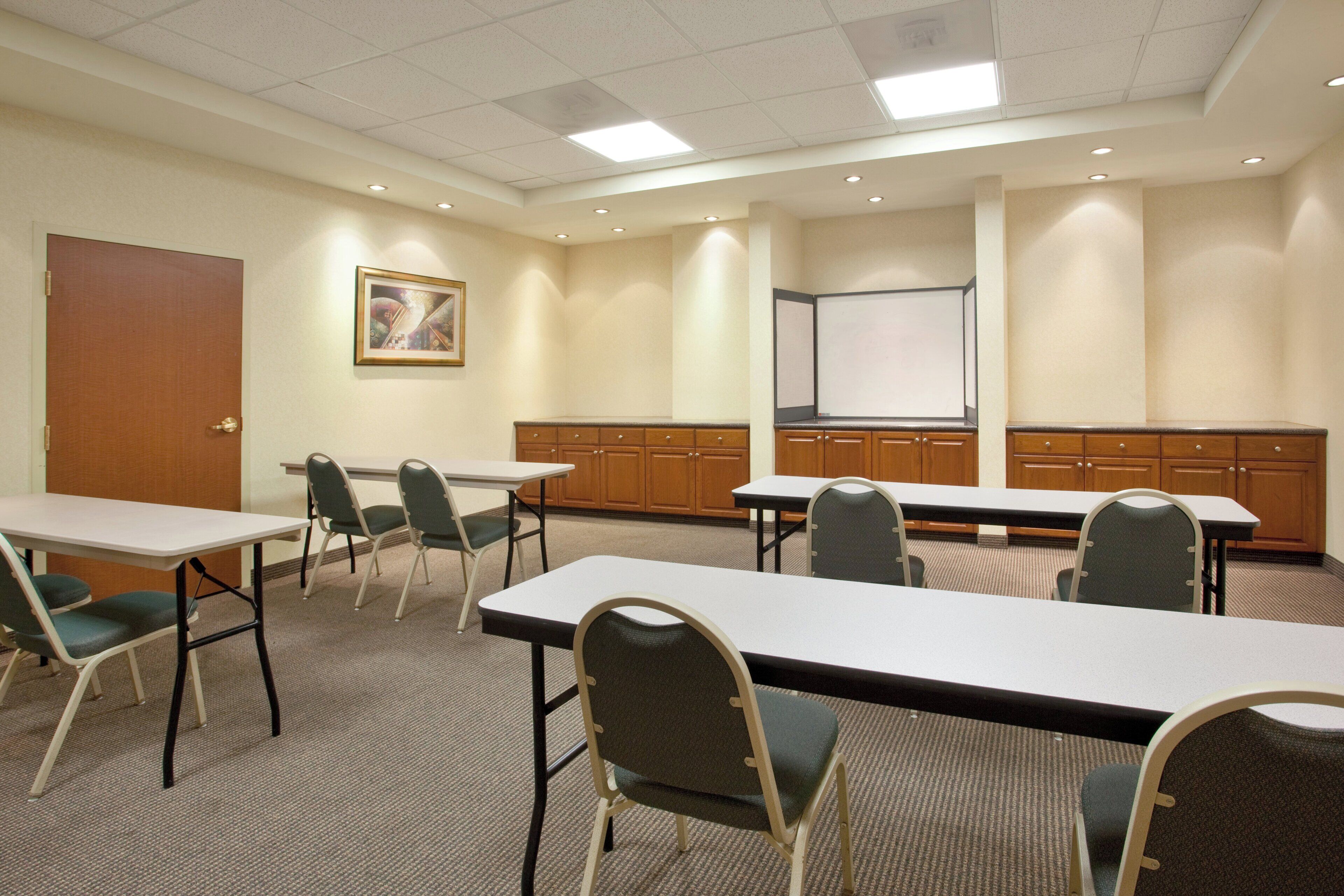 A conference room with tables, chairs, a projector screen, and a door.
