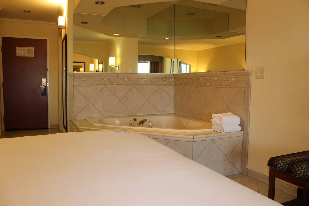 A hotel room with a large bed, a bathtub, and a mirror above the tub.