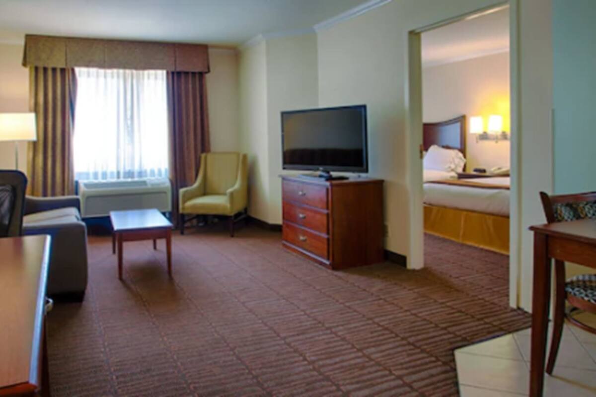 A hotel room with a bed, a television, a desk, a chair, and a window with curtains.