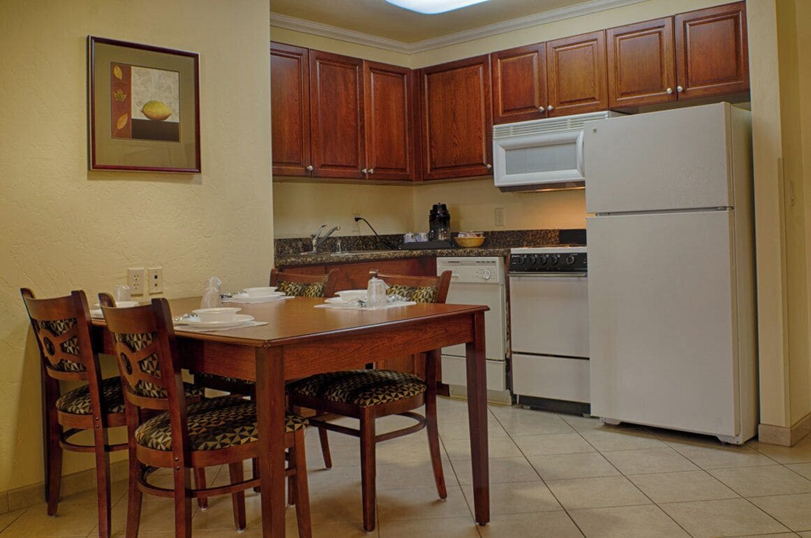 A kitchen with wooden cabinets, a white refrigerator, a dining table with chairs, and a microwave above the stove.