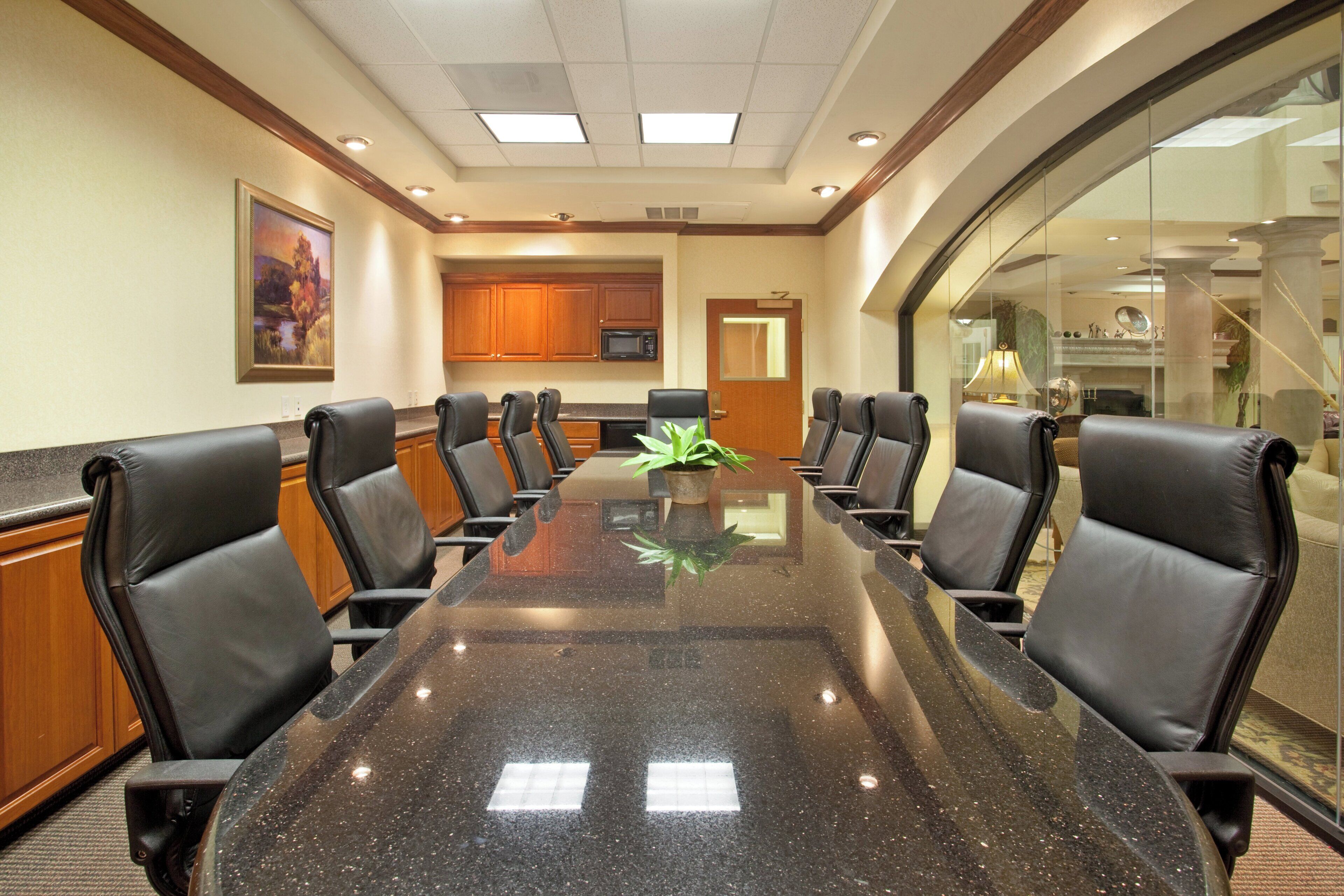 A conference room with a glass table, black leather chairs, wooden cabinets, and a painting on the wall.