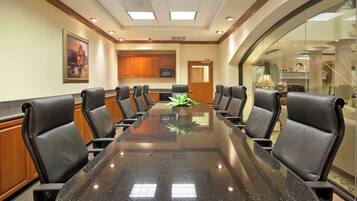 A conference room with a glass table, black leather chairs, wooden cabinets, and a painting on the wall.