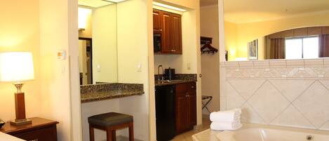 A hotel room with a large bathroom, a kitchenette, and a bed.