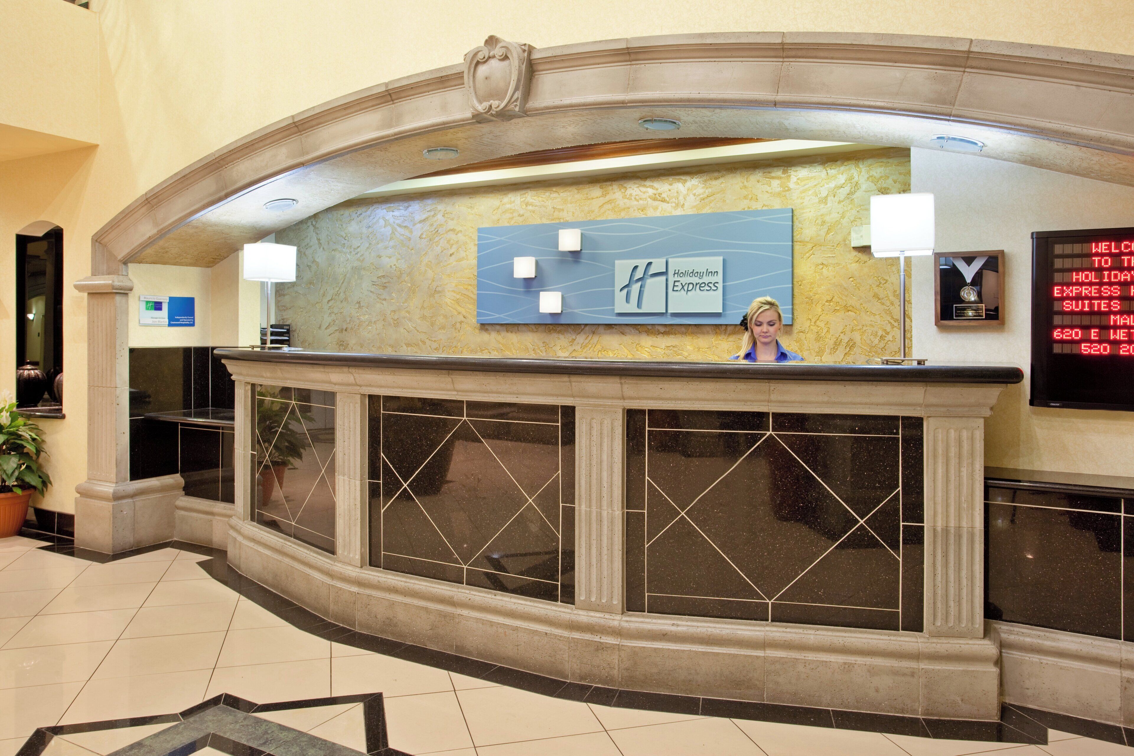 A hotel reception desk with a Holiday Inn Express sign, a digital display board, and a potted plant.