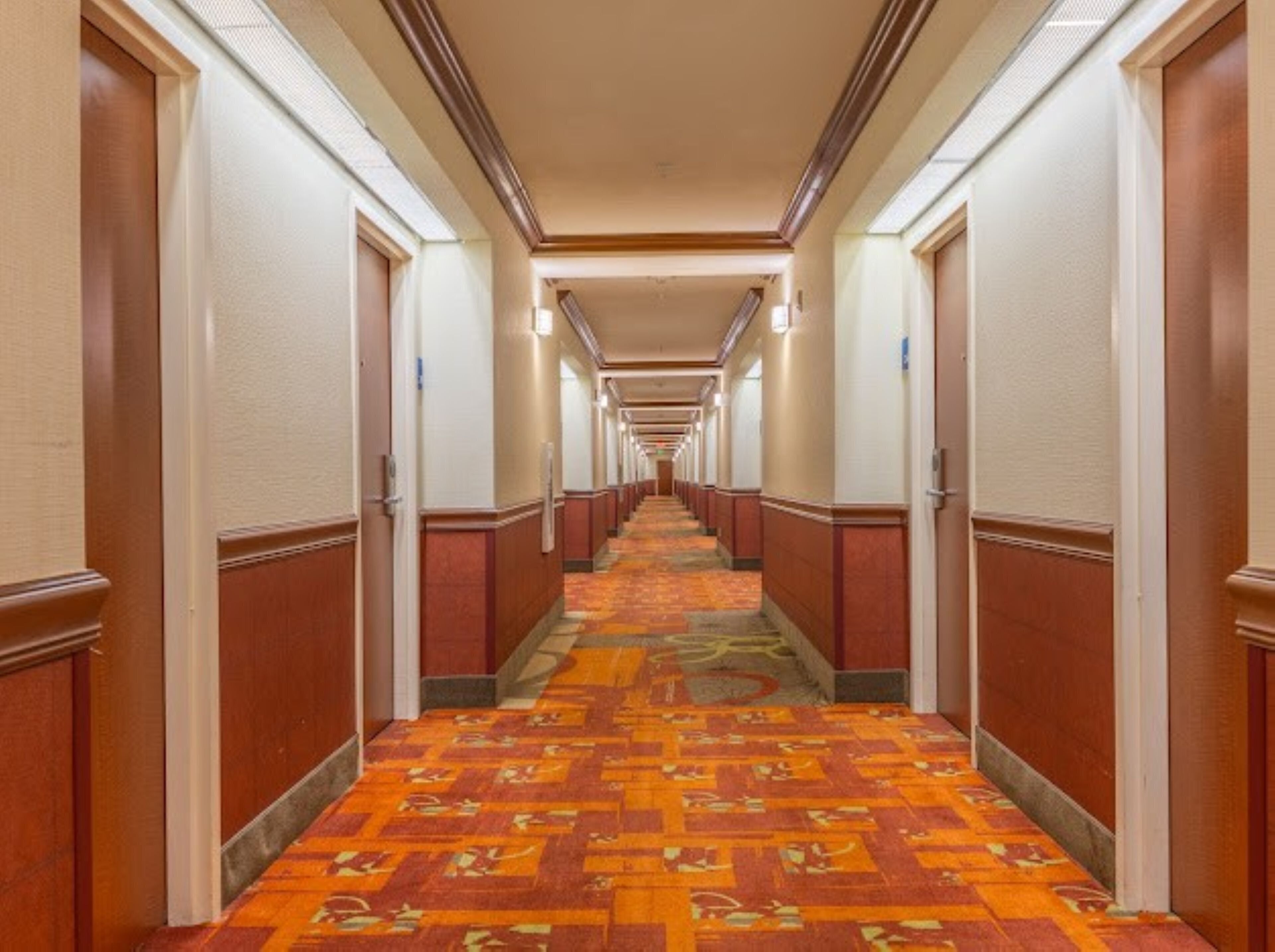 Un pasillo de hotel con pisos alfombrados, puertas de madera y una larga extensión.
