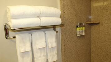 A bathroom with a towel rack holding folded towels and a shelf with toiletries.