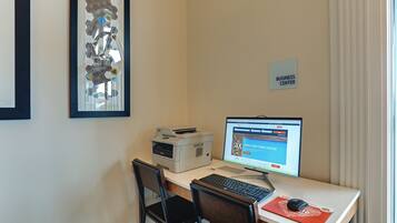 A workspace with a desktop computer, printer, and two chairs. A sign on the wall reads "BUSINESS CENTER."