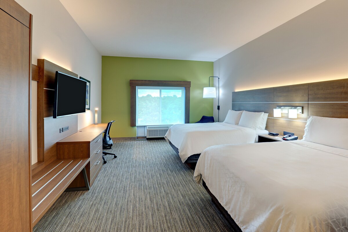 Habitación de hotel con dos camas, un escritorio, un televisor de pantalla plana, una silla y ventana con vista a  árboles.