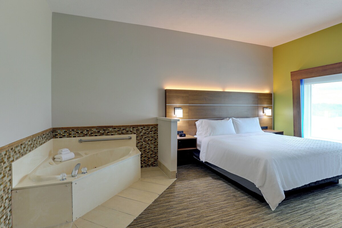 Une chambre d’hôtel avec une grande baignoire, un lit avec du linge de maison blanc et une table de chevet avec une lampe.