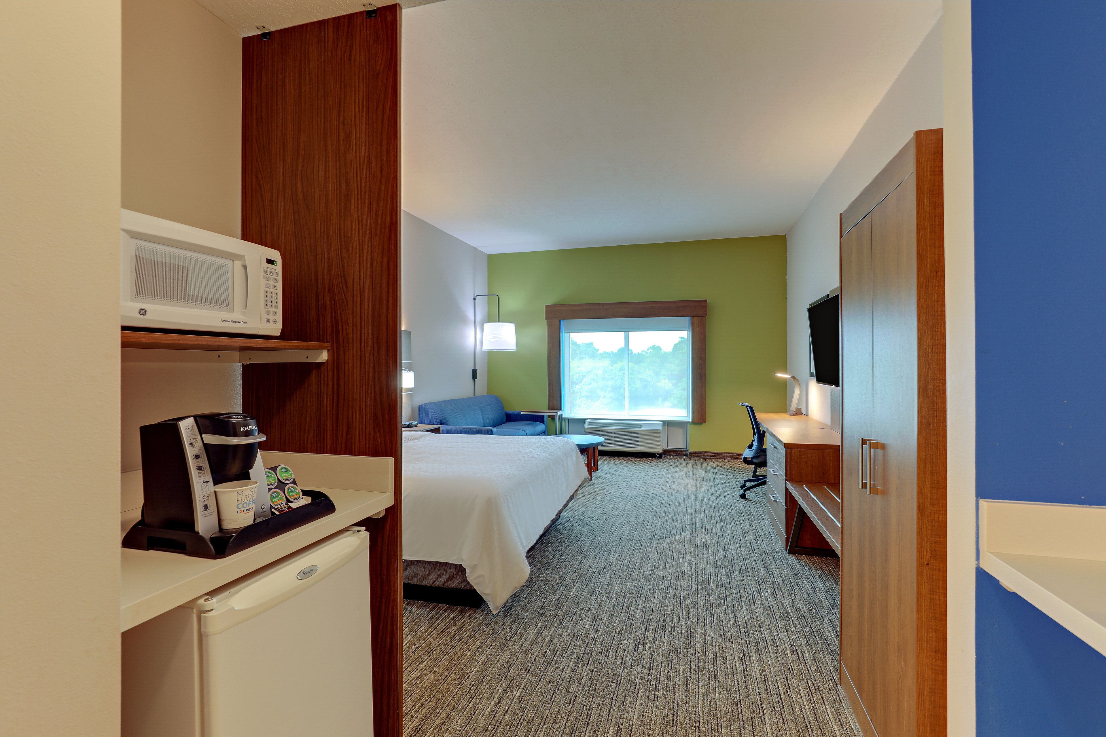 Una habitación de hotel con cama, escritorio con microondas, cafetera y televisión.
