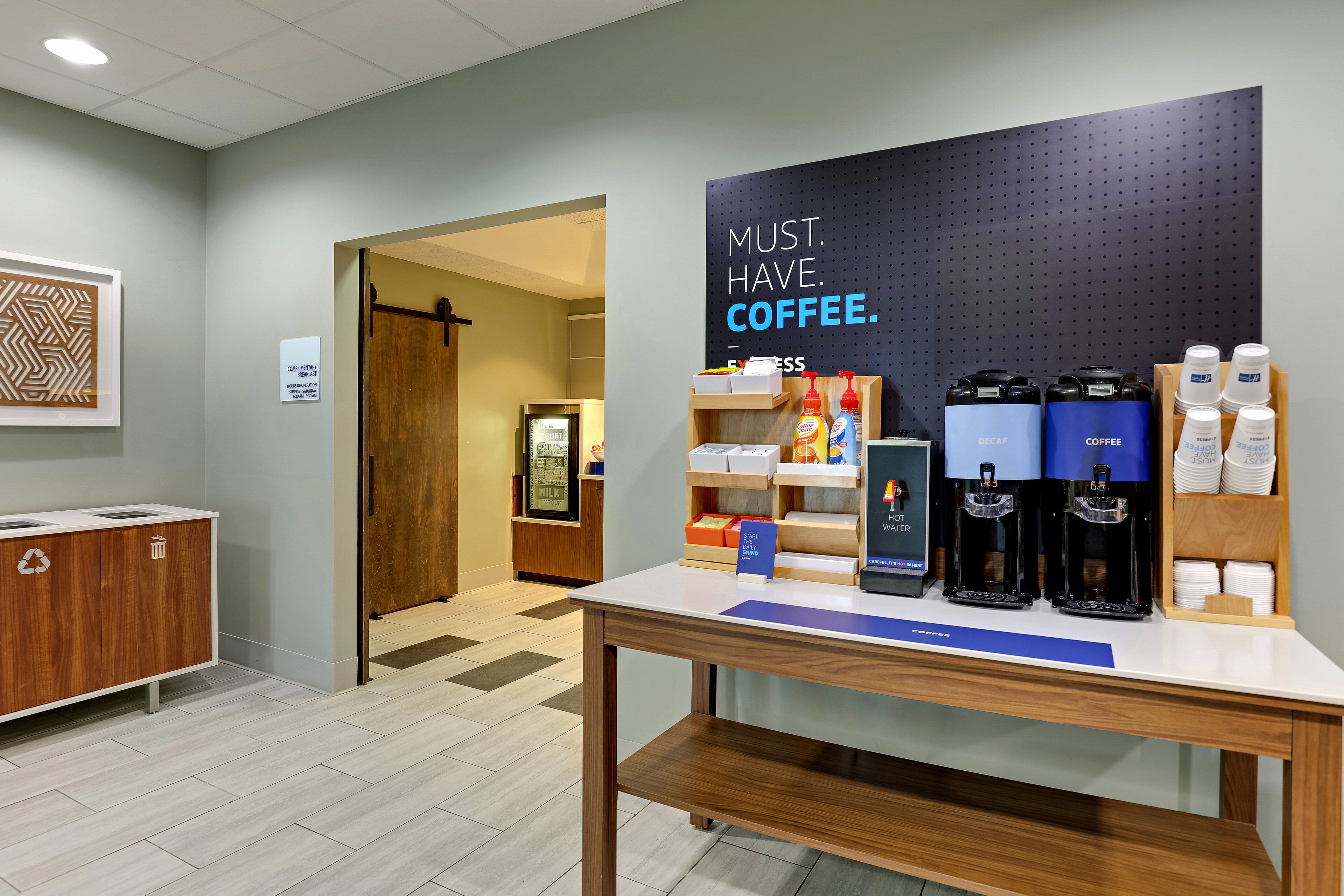 A coffee station with a sign that reads "MUST HAVE COFFEE." There are coffee makers, cups, and a display of coffee products on a table.