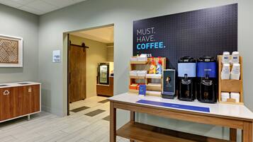A coffee station with a sign that reads "MUST HAVE COFFEE." There are coffee makers, cups, and a display of coffee products on a table.
