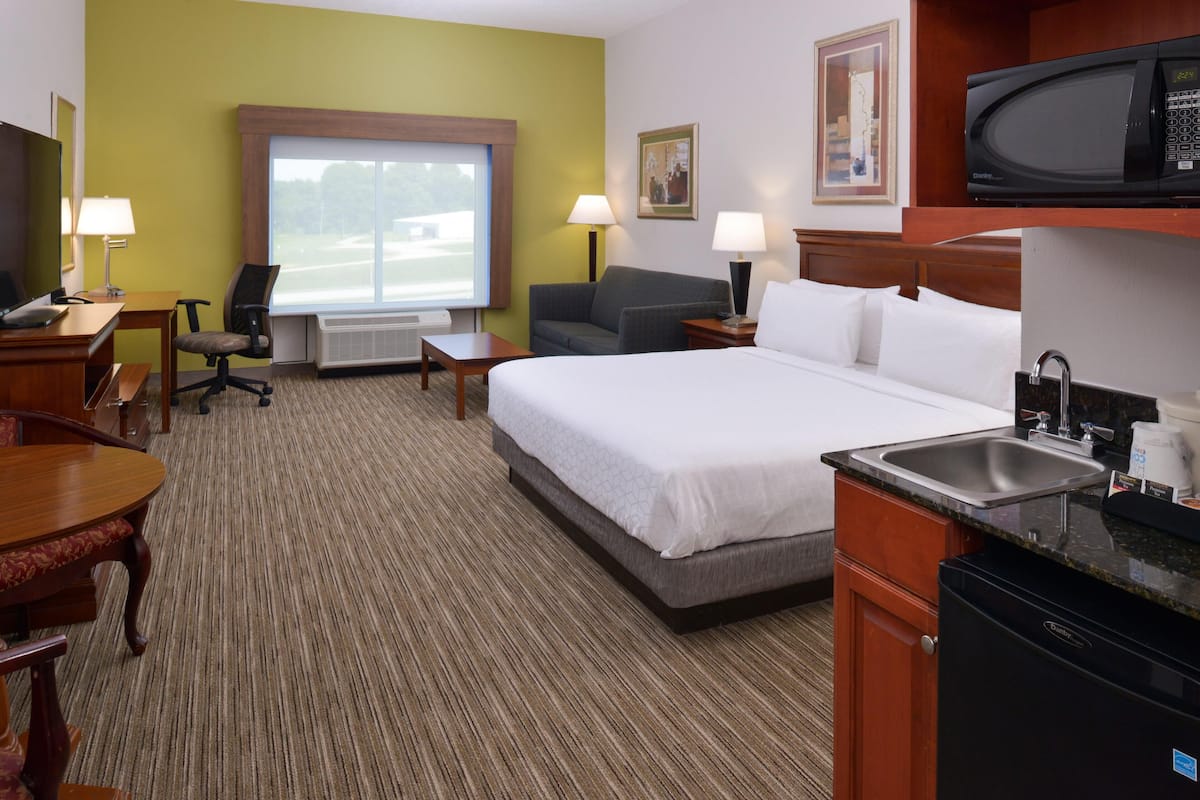 Una habitación de hotel con cama, escritorio, silla y kitchenette.