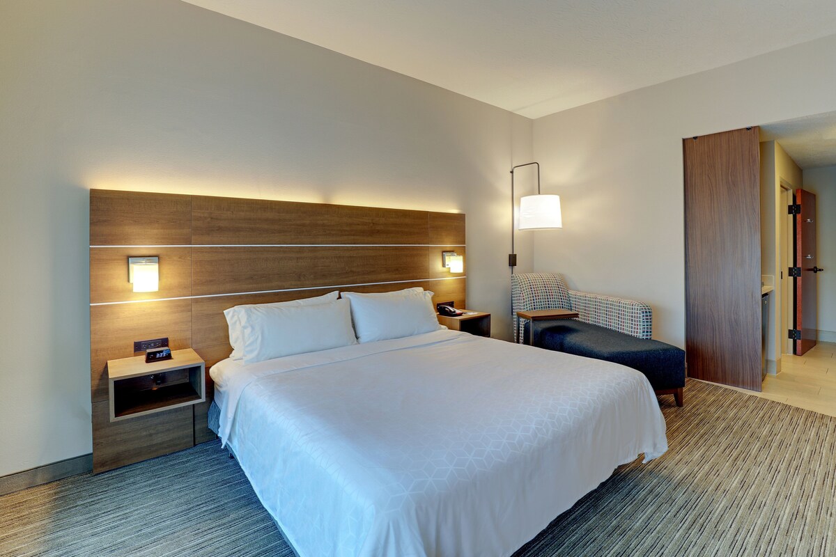 Una habitación de hotel con una cama grande, una mesita de noche, una lámpara, una silla y un armario.
