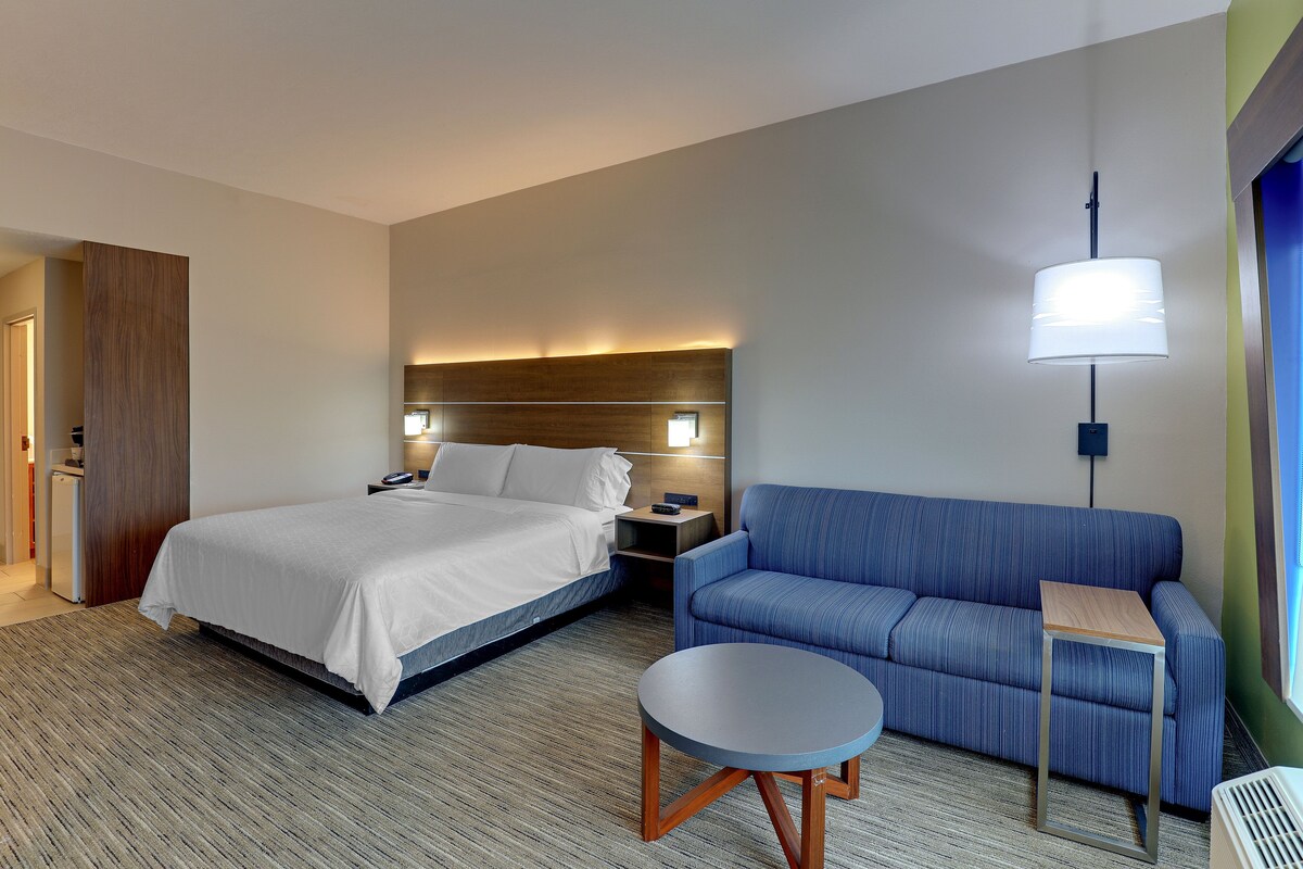 Una habitación de hotel con una cama, un sofá azul, una mesita, una lámpara y una mesita de noche.