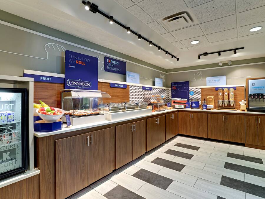 A modern breakfast area with a fruit display, hot food station, and a refrigerated section.