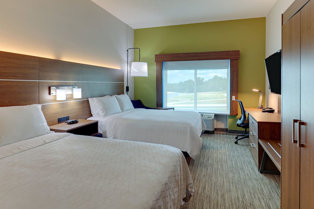 Habitación de hotel con dos camas, un escritorio, una silla, un televisor y una ventana con vista a un campo.