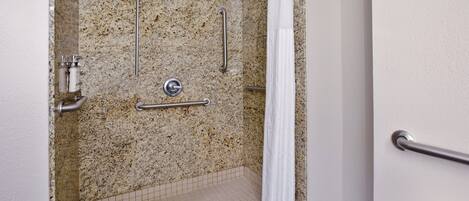 A handicap-accessible shower with grab bars, a showerhead, and a white curtain.