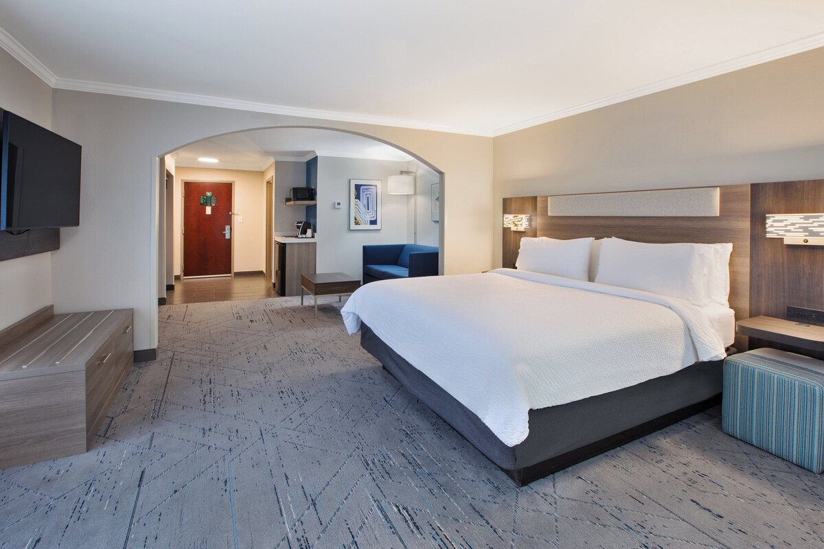 A hotel room with a large bed, a TV mounted on the wall, a desk, and a chair.