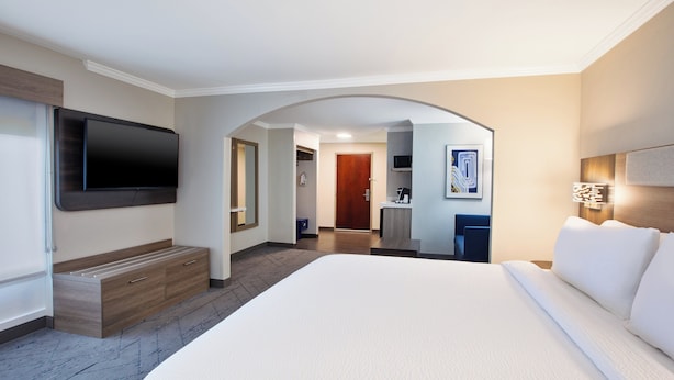 A hotel room with a large bed, a flat-screen TV mounted on the wall, a wooden bench, and a desk with a chair. - Holiday Inn Express Sumter by IHG (Sumter)