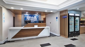 A hotel reception area with a modern design, including a reception desk, a digital display, and a refrigerator stocked with snacks. - Holiday Inn Express Sumter by IHG (Sumter)