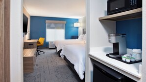 A hotel room with a bed, a desk, a chair, a microwave, a coffee machine, and a mini-fridge.