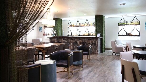 A modern restaurant with a bar area, wooden flooring, and a variety of seating options including tables and chairs.
