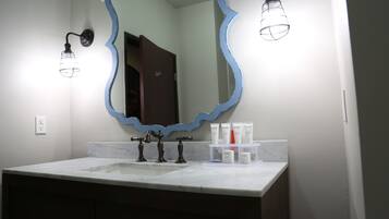 A bathroom with a marble sink, two black faucets, a blue-framed mirror, and a shelf with toiletries.