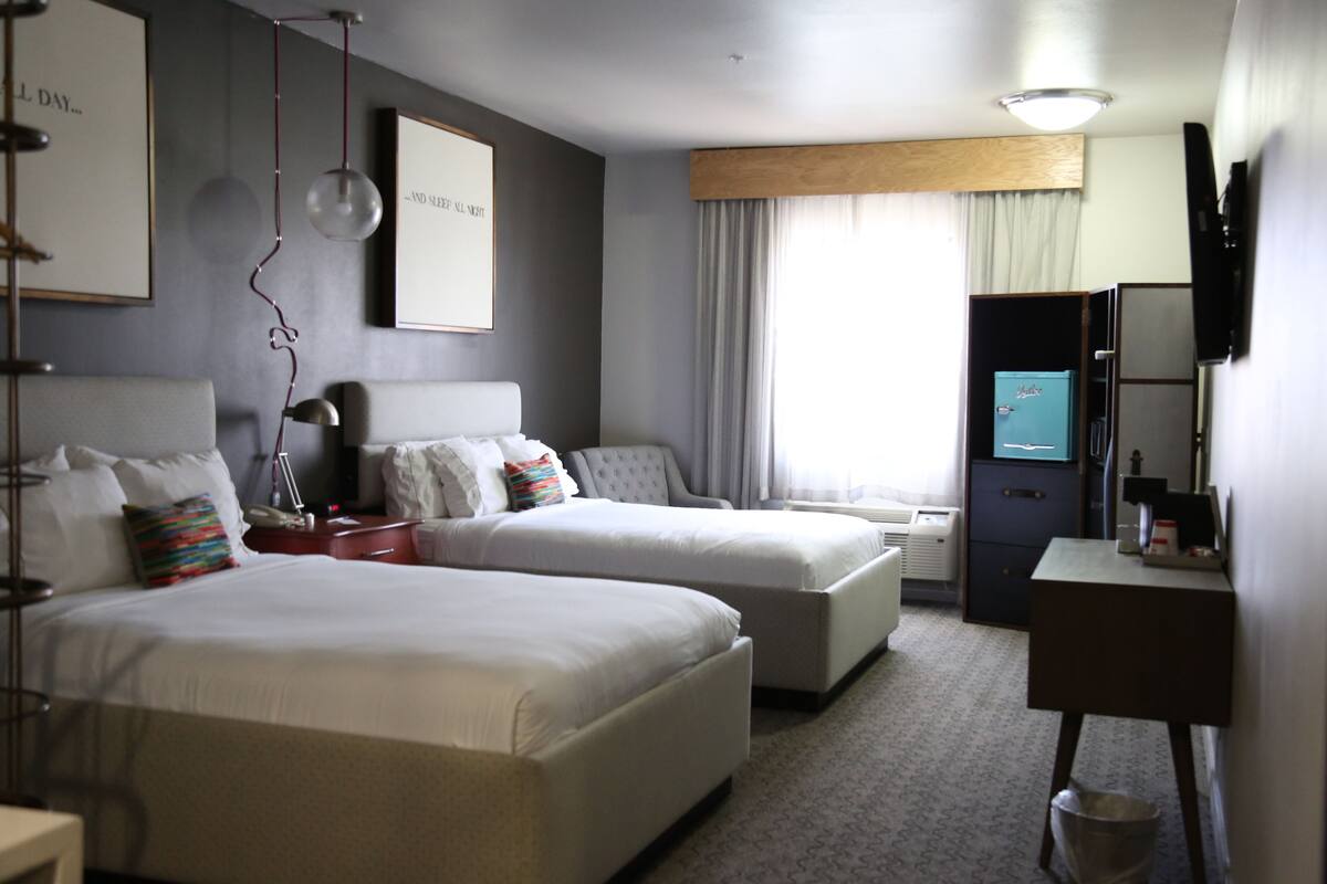 A hotel room with two beds, a desk, a TV, and a minibar.