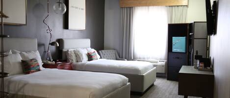 A hotel room with two beds, a desk, a TV, and a minibar.