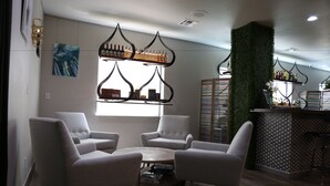 A modern interior with a seating area, a bar with a green wall, and a window with artwork.