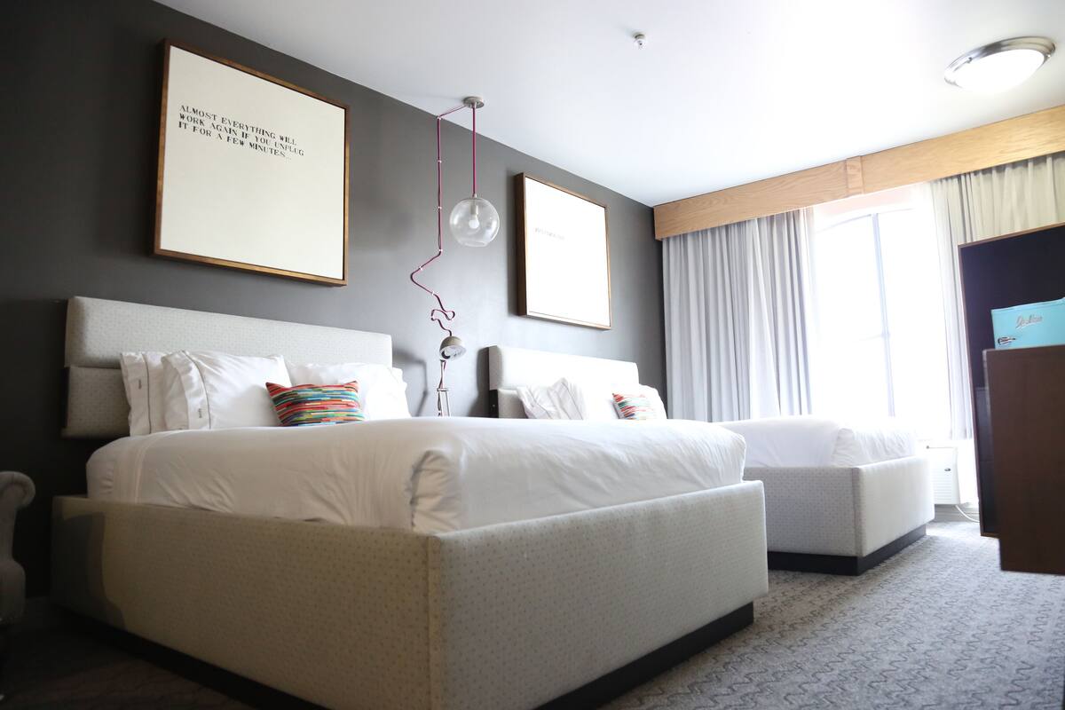 A modern hotel room with a large bed, a smaller sofa, and a desk.