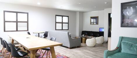 Uma sala de estar moderna com uma mesa de jantar de madeira, cadeiras pretas, um sofá cinza e uma poltrona verde.
