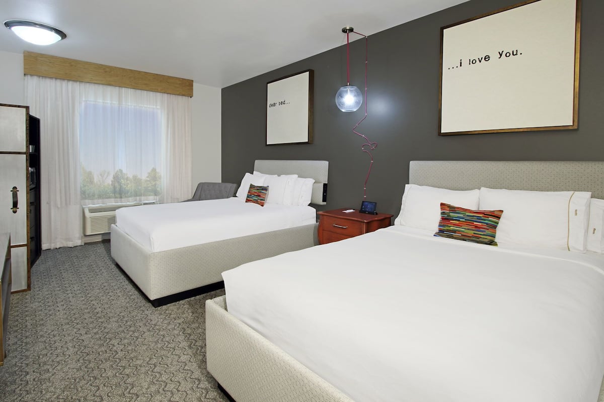 A hotel room with two beds, a desk, a wardrobe, and a window with curtains.