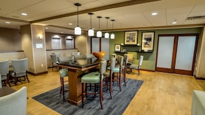 A hotel breakfast area with a bar, seating, and a view of the kitchen. - Hampton Inn Ft Payne (Fort Payne)